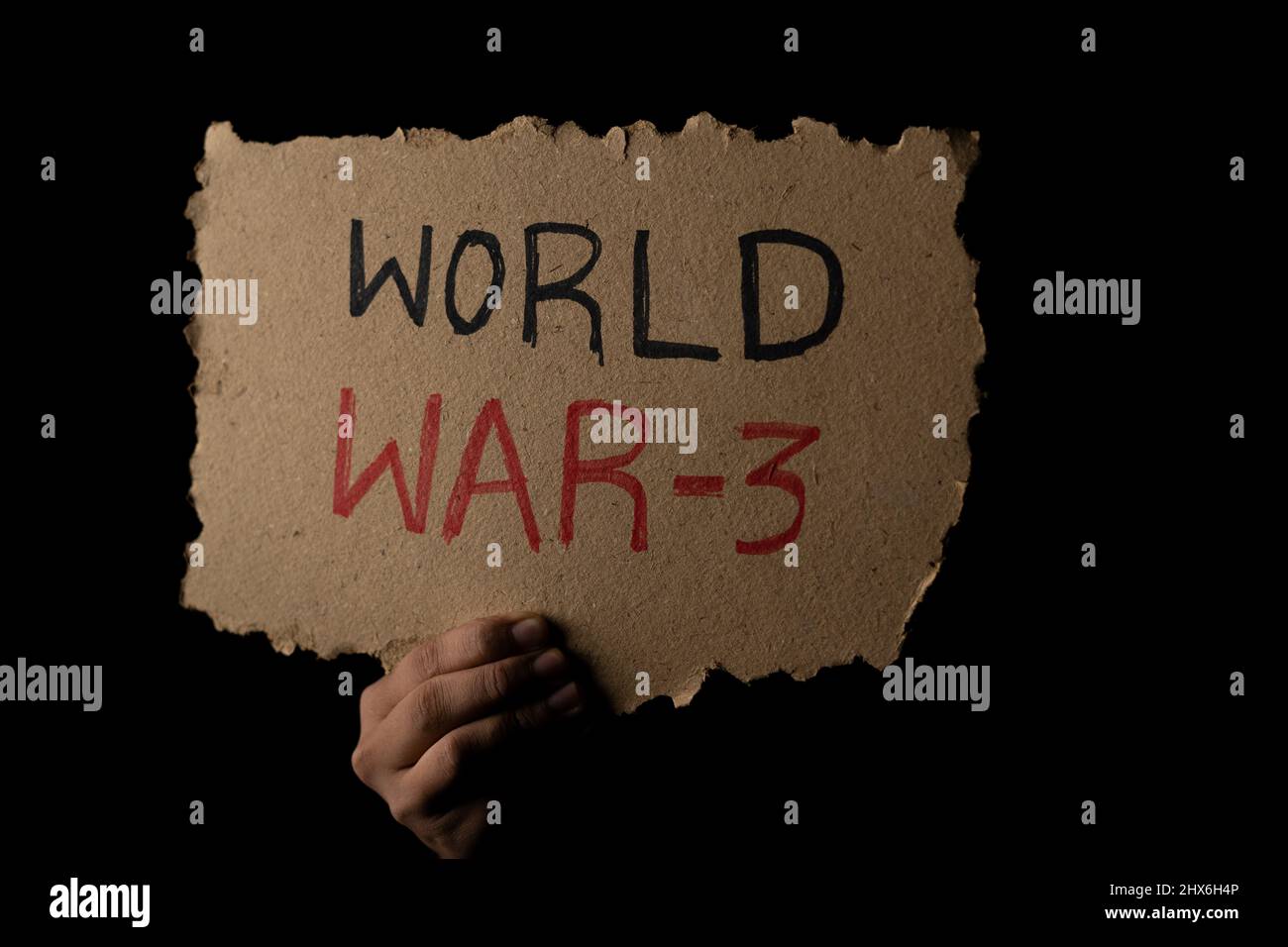 close up hands holding World War 3 sign board or placard on dark background - concept of conflicts, political crisis and demonstration. Stock Photo