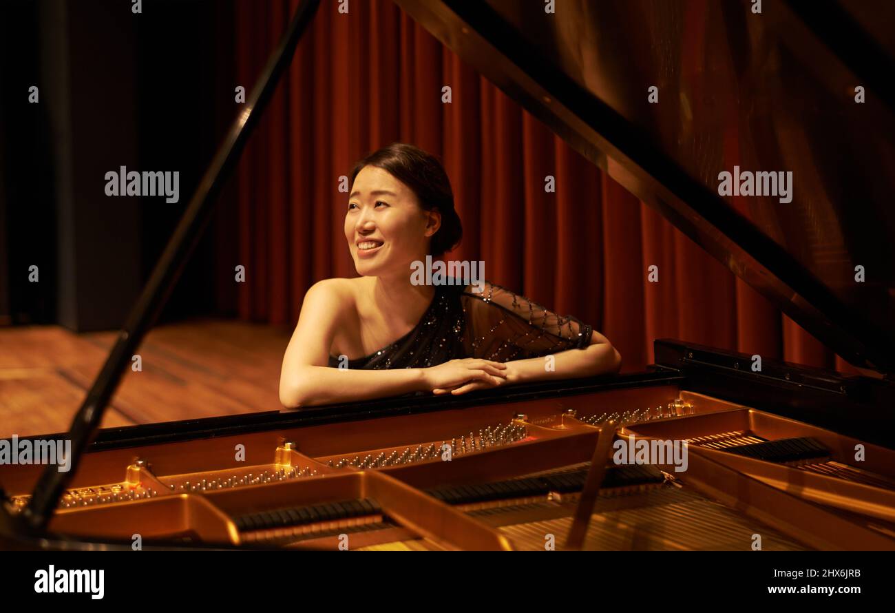 Appreciating the crowd. Shot of a young woman sitting by her piano at the end of a musical concert. Stock Photo