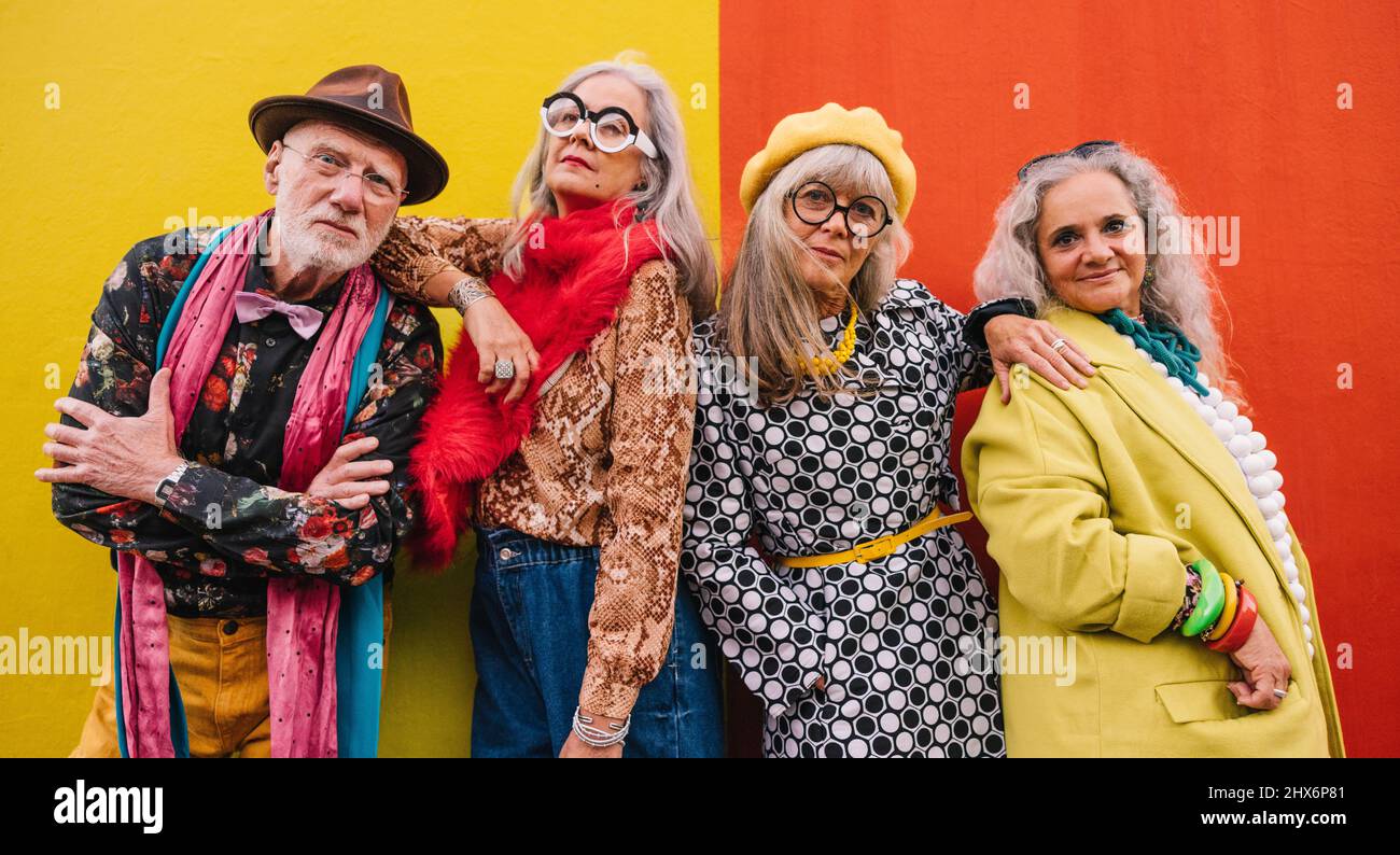 Active elderly people looking at the camera while standing together against a colourful wall. Group of four senior citizens feeling confident and yout Stock Photo