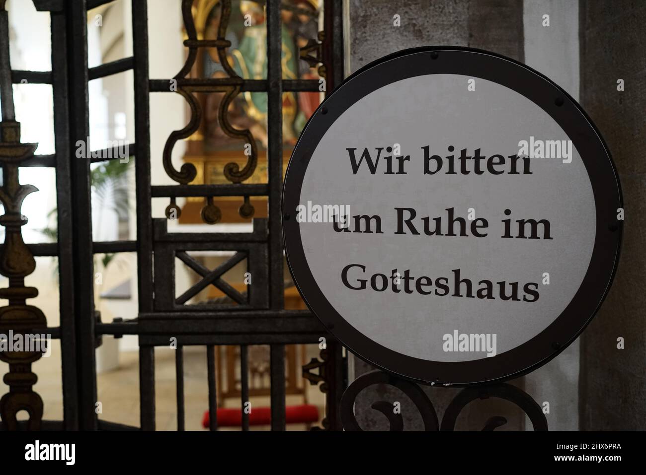 A plate with text in German. 'Wir bitten um Ruhe im Gotteshaus' means: We ask for silence in the church. In the background a blurred church interior Stock Photo
