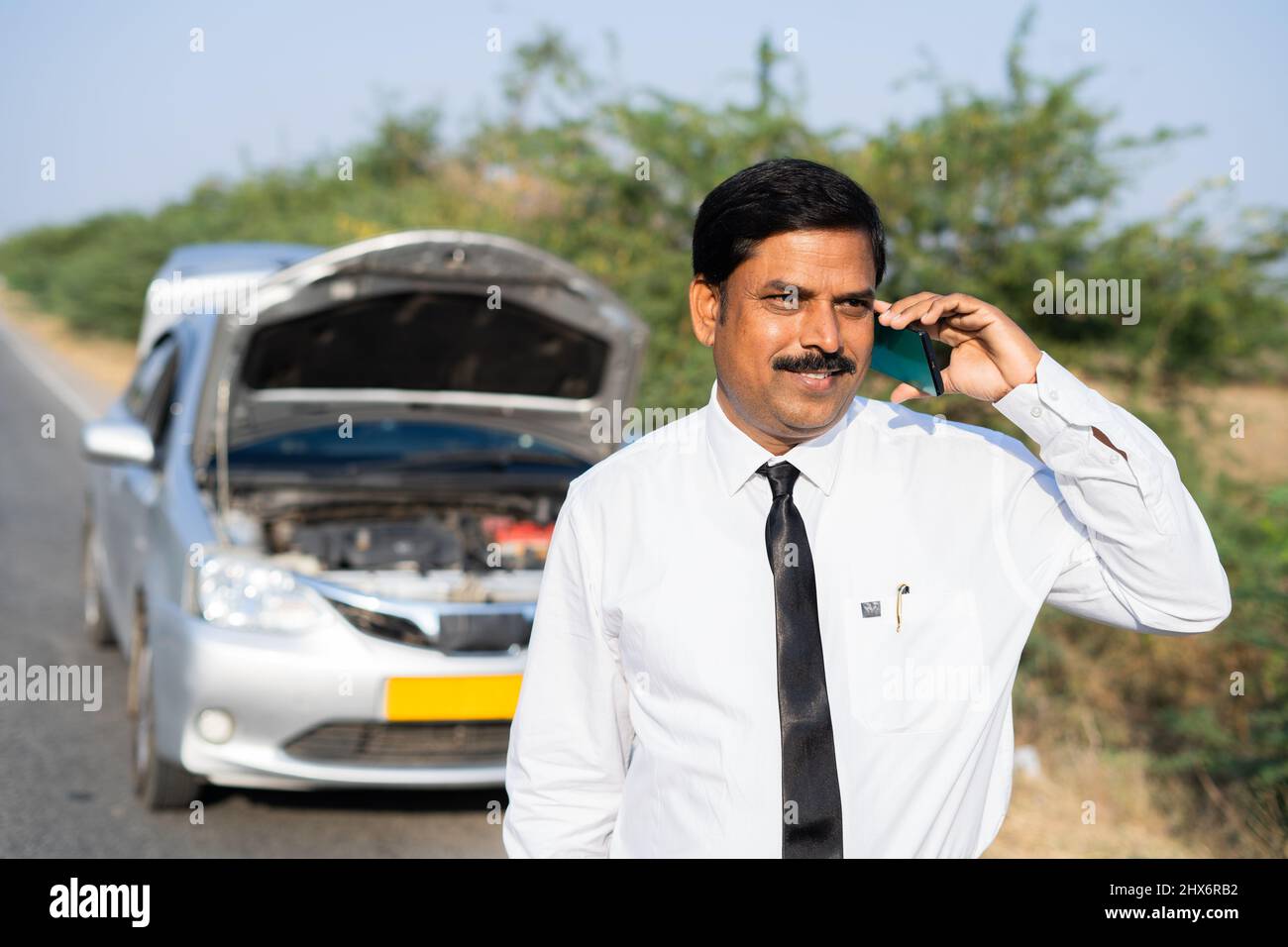 Businessman talking on mobile phone with car mechanic while car breakdown at highway road - concept of communication, car repair service and Stock Photo