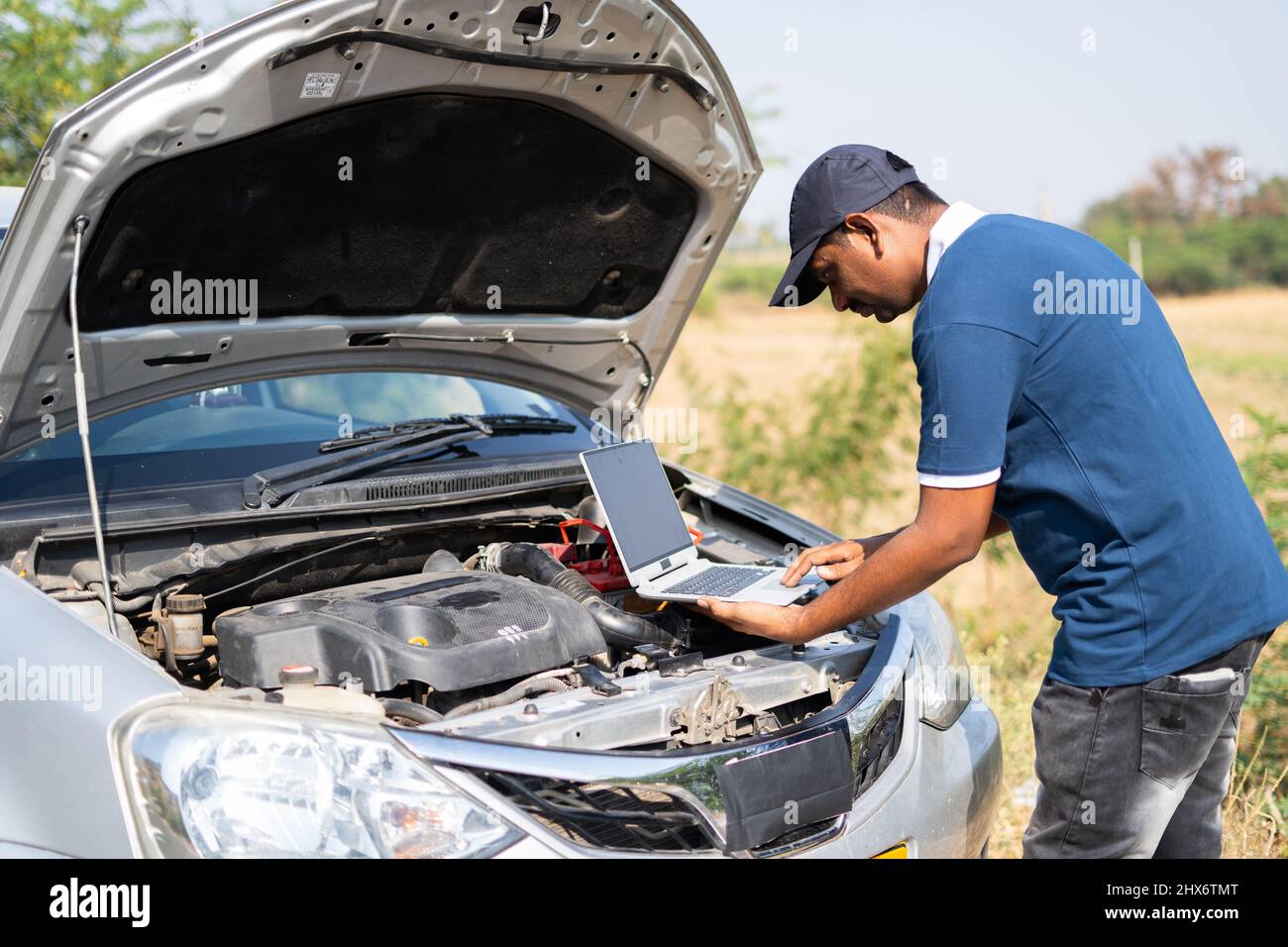 professional mechanic using laptop for checking car by lifting car hood