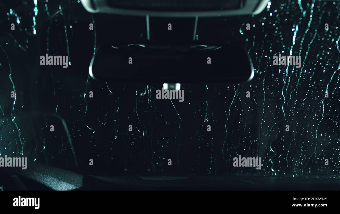Drops flow down the windscreen. Inside view of a windshield car. Dark black cinematic picture. Process stage of polishing and washing a auto. Movement zoom camera dolly shooting platform. Stock Photo