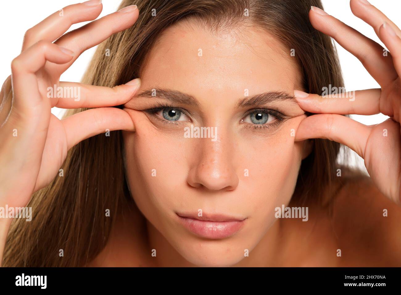 a young woman squeezes the wrinkles aroud her eyes on white background Stock Photo