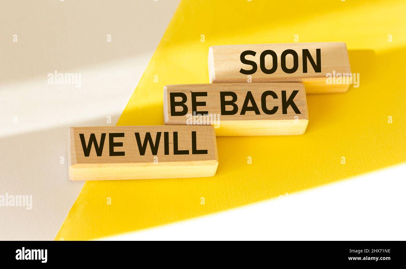 We'll be back soon, text on wooden blocks and white and yellow background Stock Photo