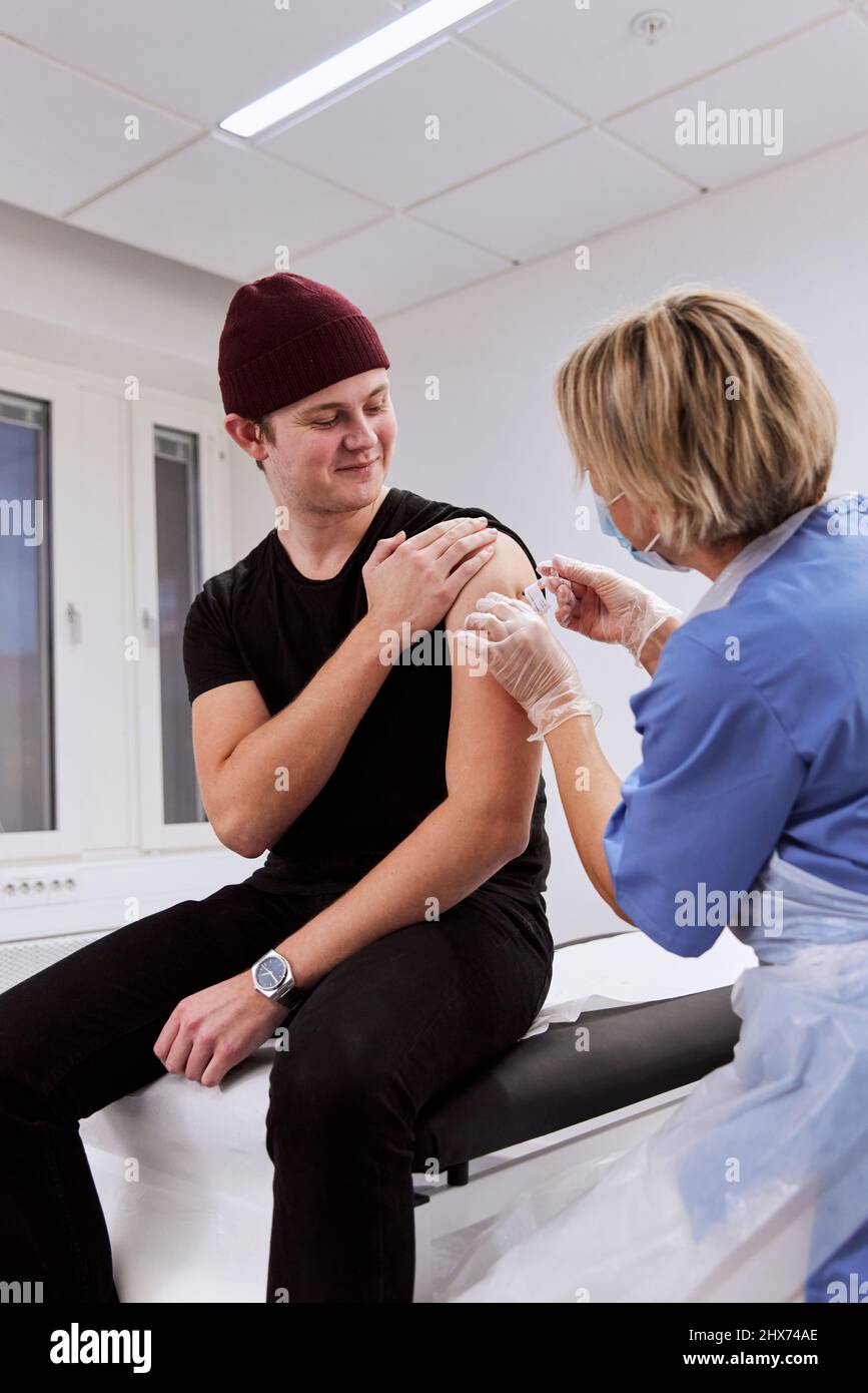 Smiling young man getting vaccinated against Covid-19 Stock Photo