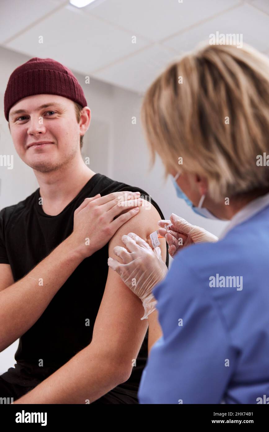 Smiling young man getting vaccinated against Covid-19 Stock Photo