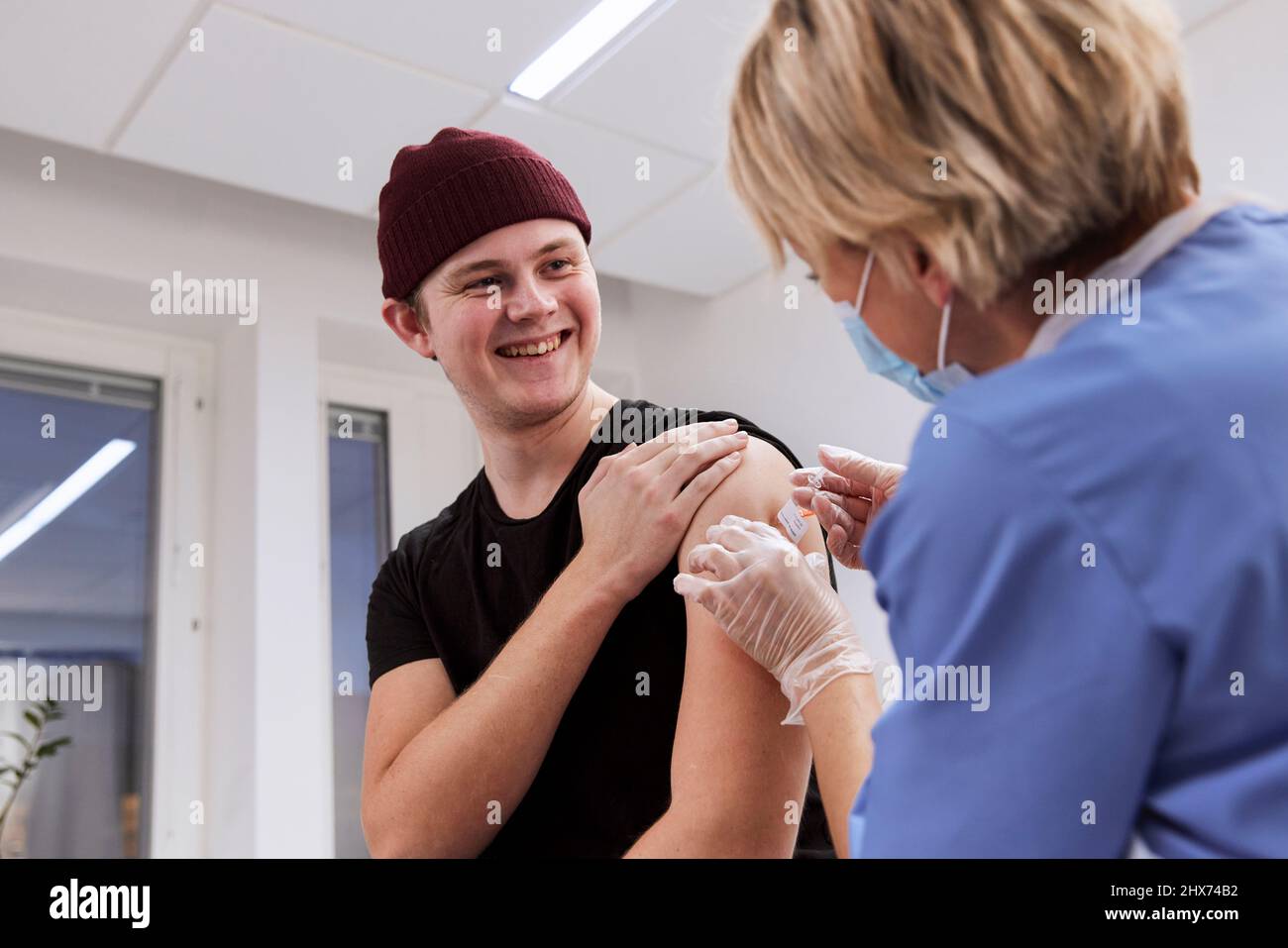 Smiling young man getting vaccinated against Covid-19 Stock Photo