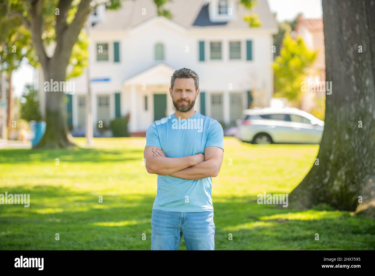 confident unshaven guy standing near new home, buying house Stock Photo