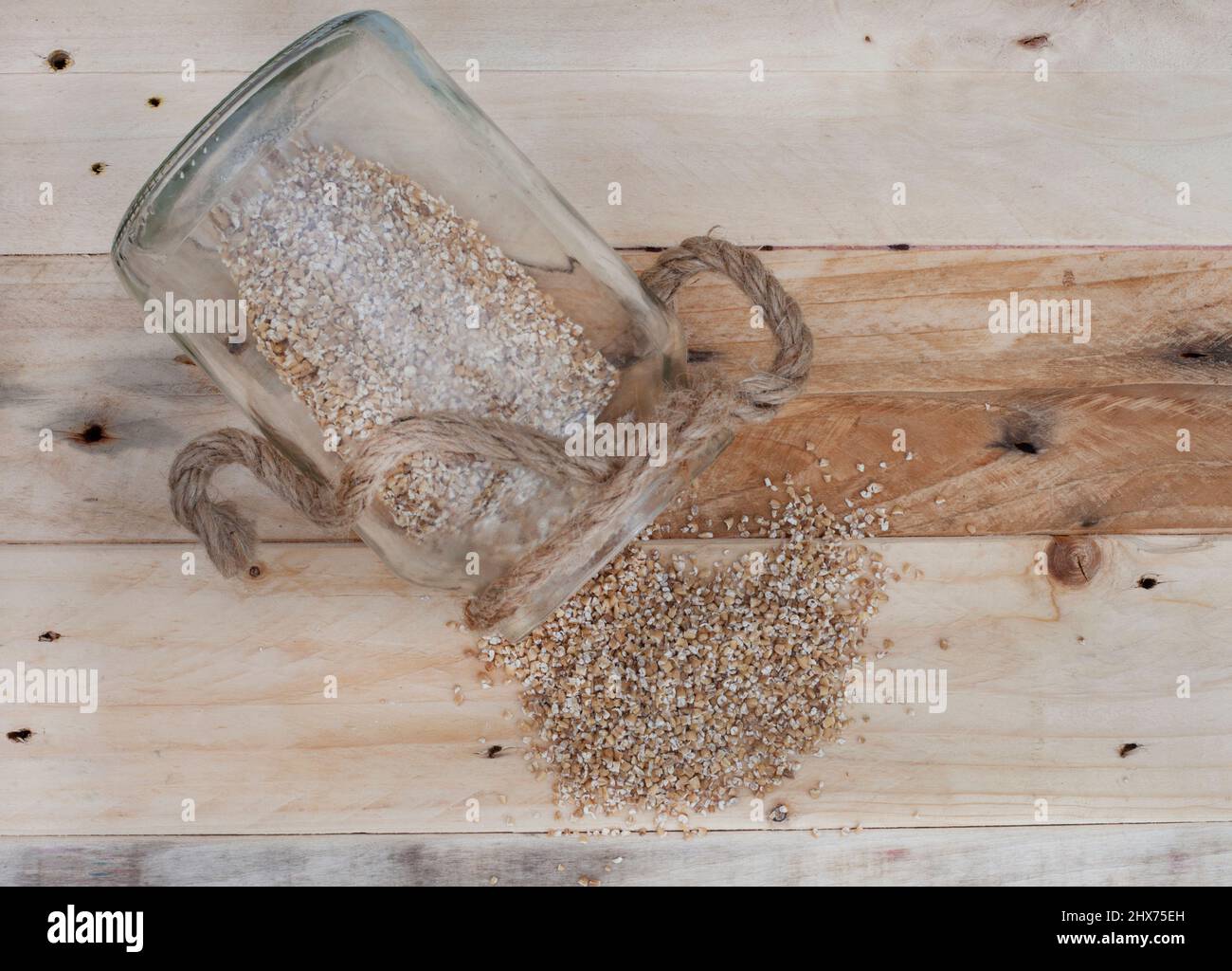 steel cut oats spilling out of almost empty jar on rustic wooden table Stock Photo