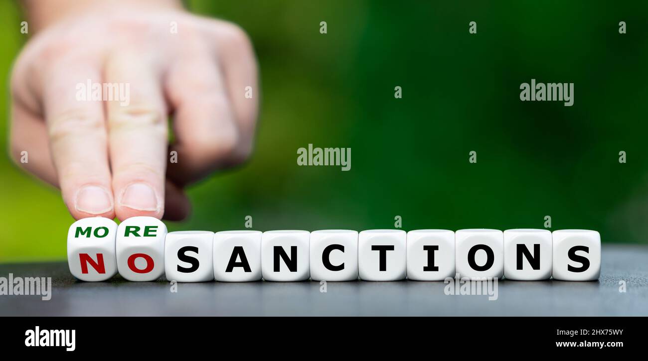 Hand turns dice and changes the expression 'no sanctions' to 'more sanctions'. Stock Photo