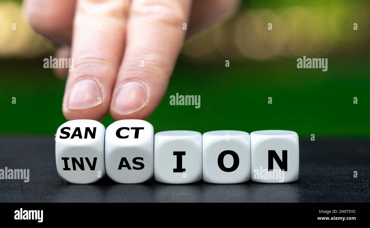 Hand turns dice and changes the word invasion to sanction. Stock Photo