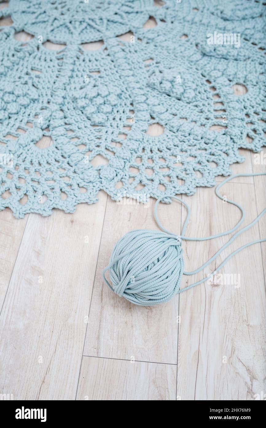 Handmade carpet knitted from natural threads, flooring, natural cotton. Beige handmade carpet. Knitted decorative item. Skein of blue knitting thread Stock Photo