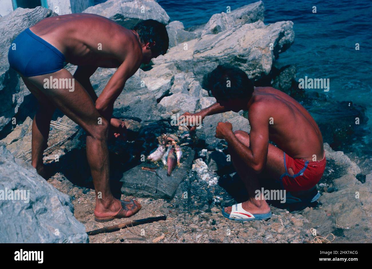 Fisherman cooking fish on open fire, Symi, Greek Islands Stock Photo