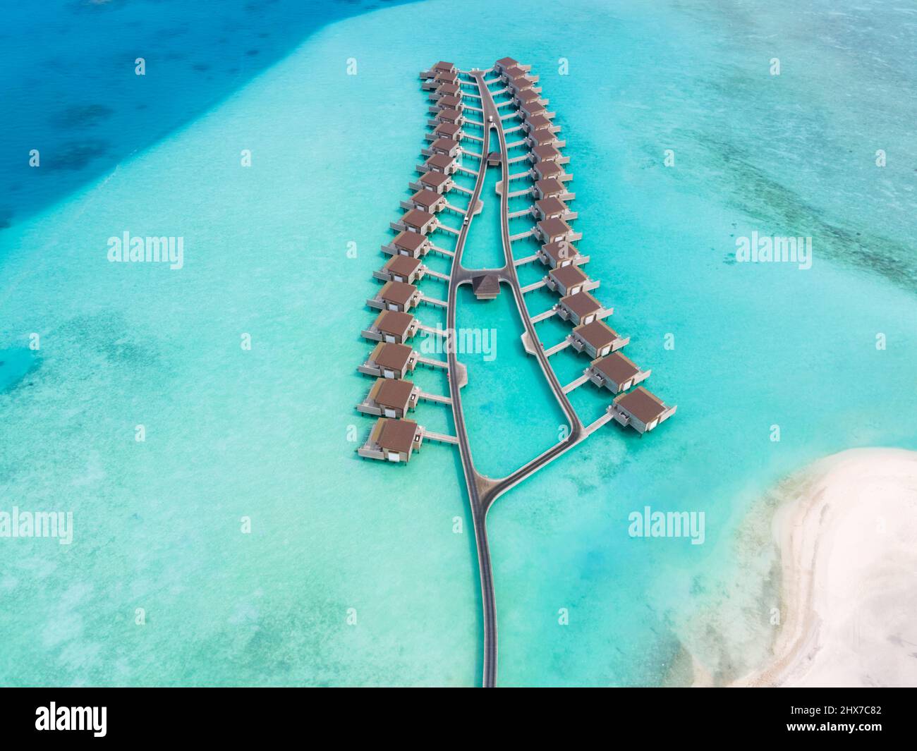 Overwater villas and white sand beach on tropical atoll island for holidays vacation travel and honeymoon. Luxury resort hotel in Maldives or Caribbea Stock Photo