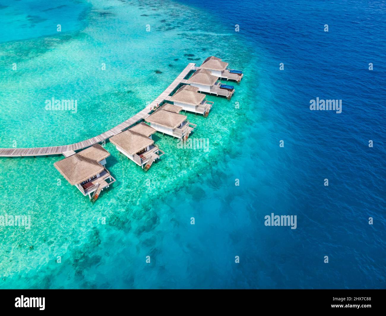 Overwater villas on tropical atoll island for holidays vacation travel and honeymoon. Luxury resort hotel in Maldives or Caribbean with turquoise sea Stock Photo