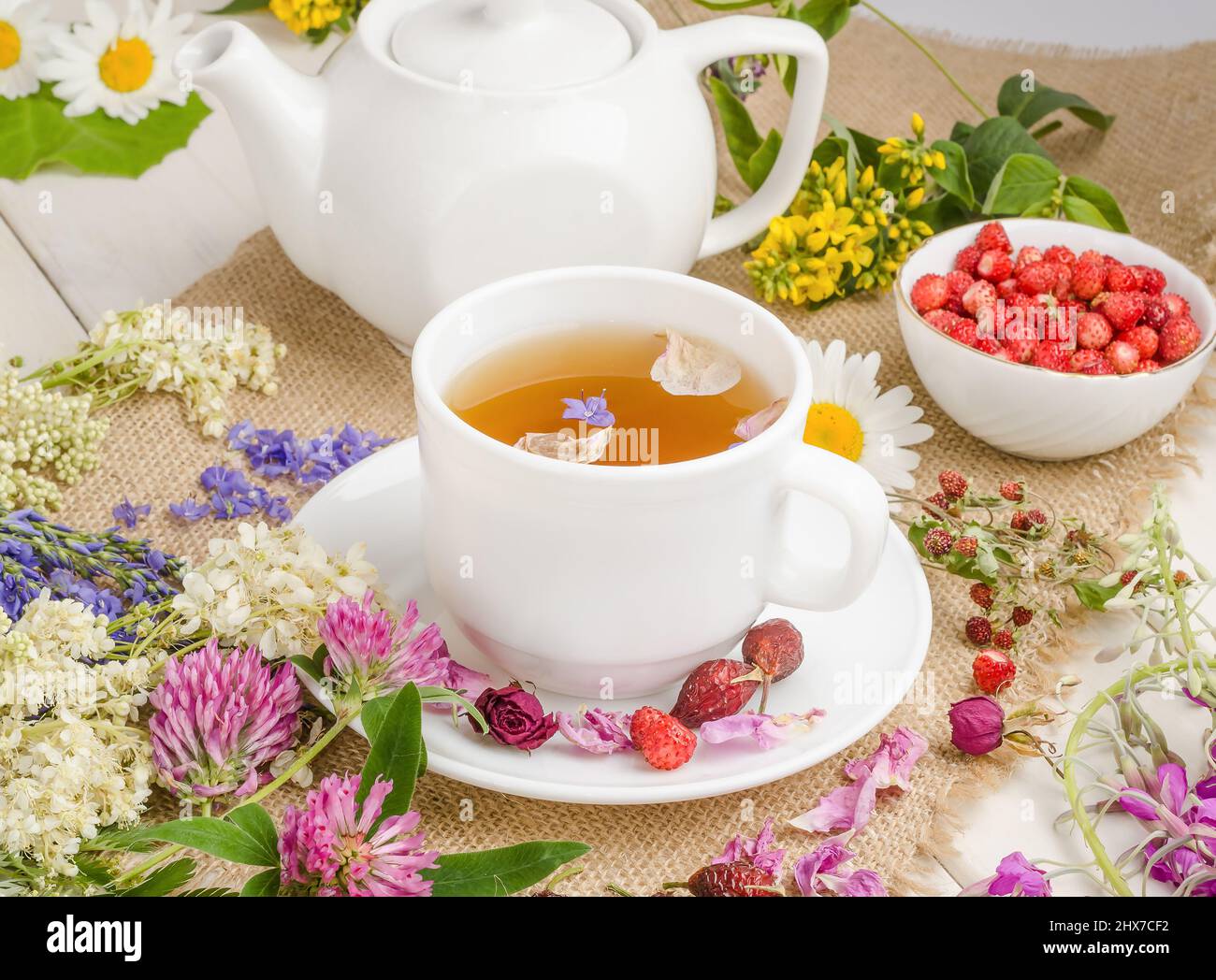 Herbal tea with rosehip, chamomile and clover in a white cup on a white wooden table with flowers. Stock Photo