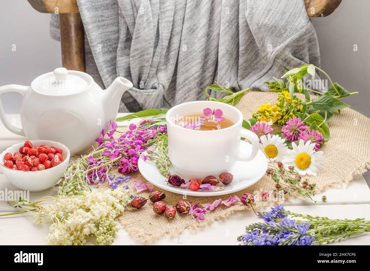 Herbal tea with rosehip, chamomile and clover in a white cup on a white wooden table with flowers. Stock Photo