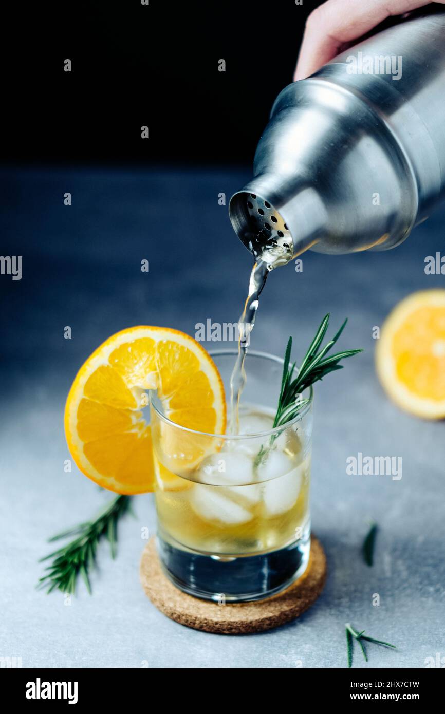 Alcohol cocktail pouring from shaker into glass with orange slice