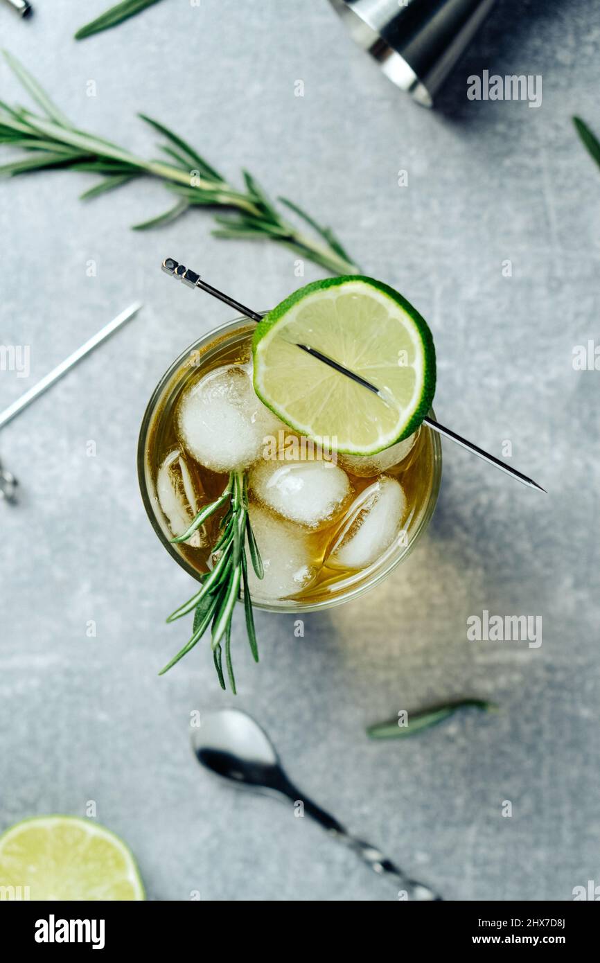 Alcohol cocktail with lime slice rosemary ice and cocktail jigger on