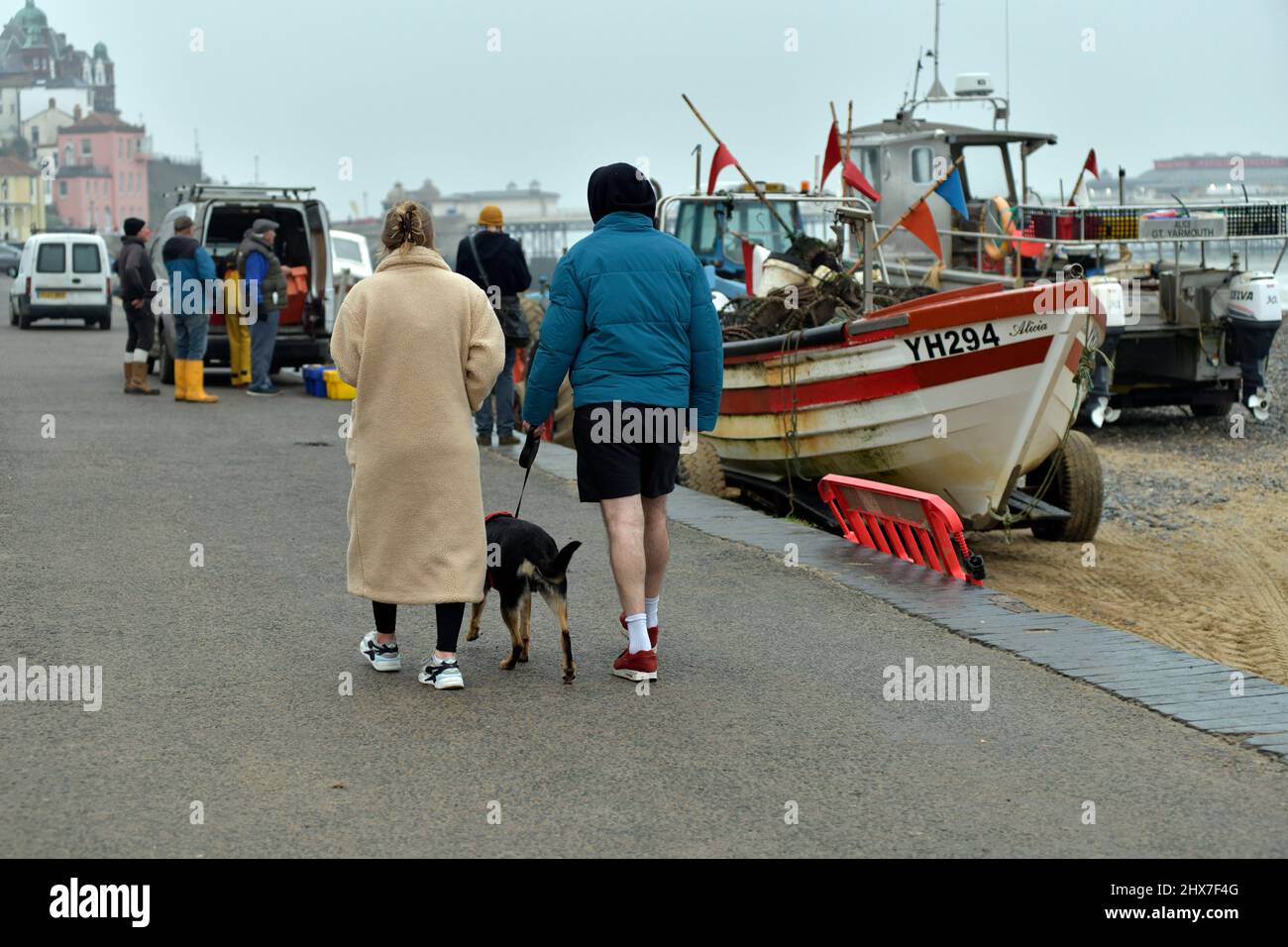 man and women walking dog along promenade near unloading fishermen cromer norfolk england Stock Photo