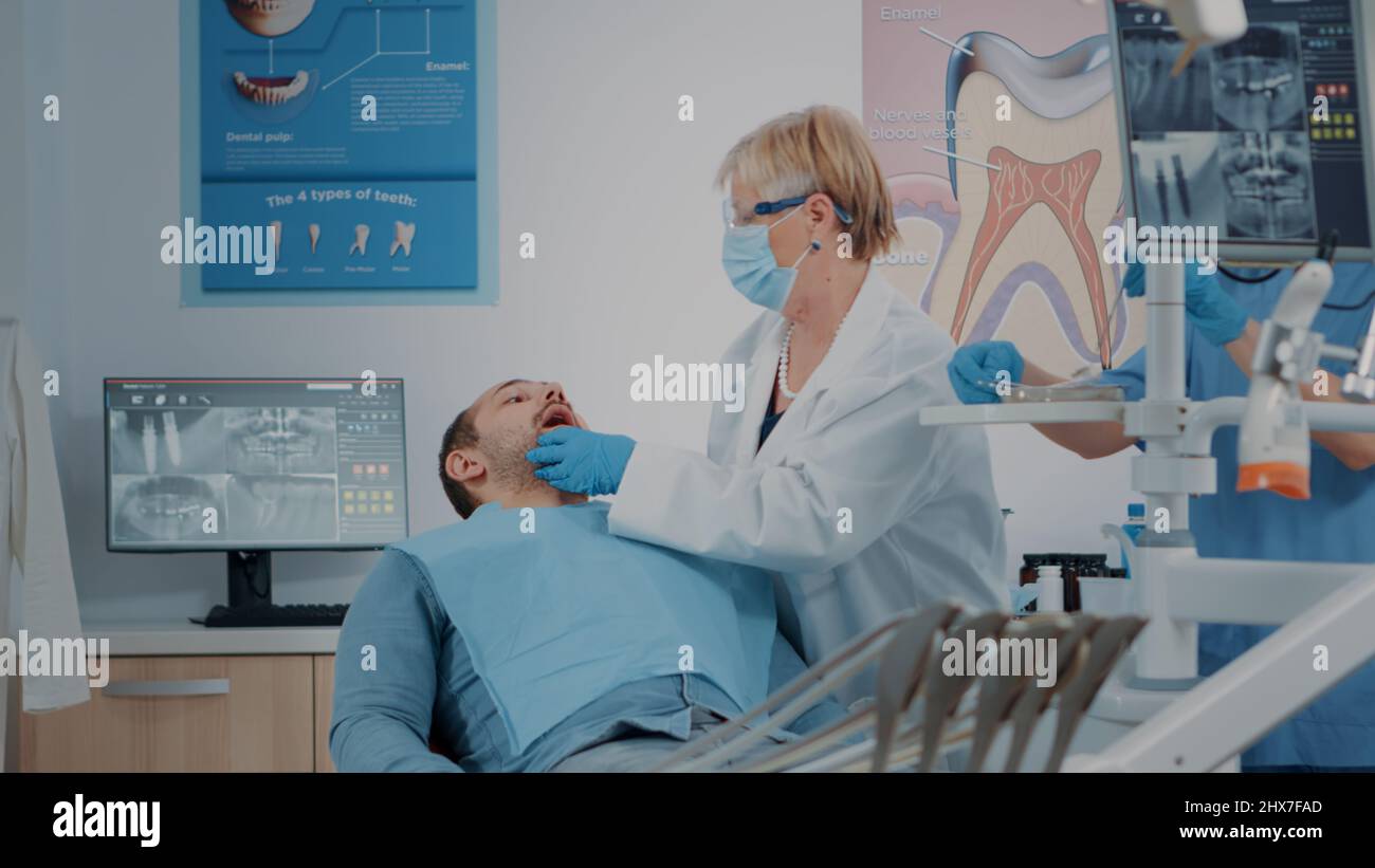 Dentist with face mask using dental tools to examine denture