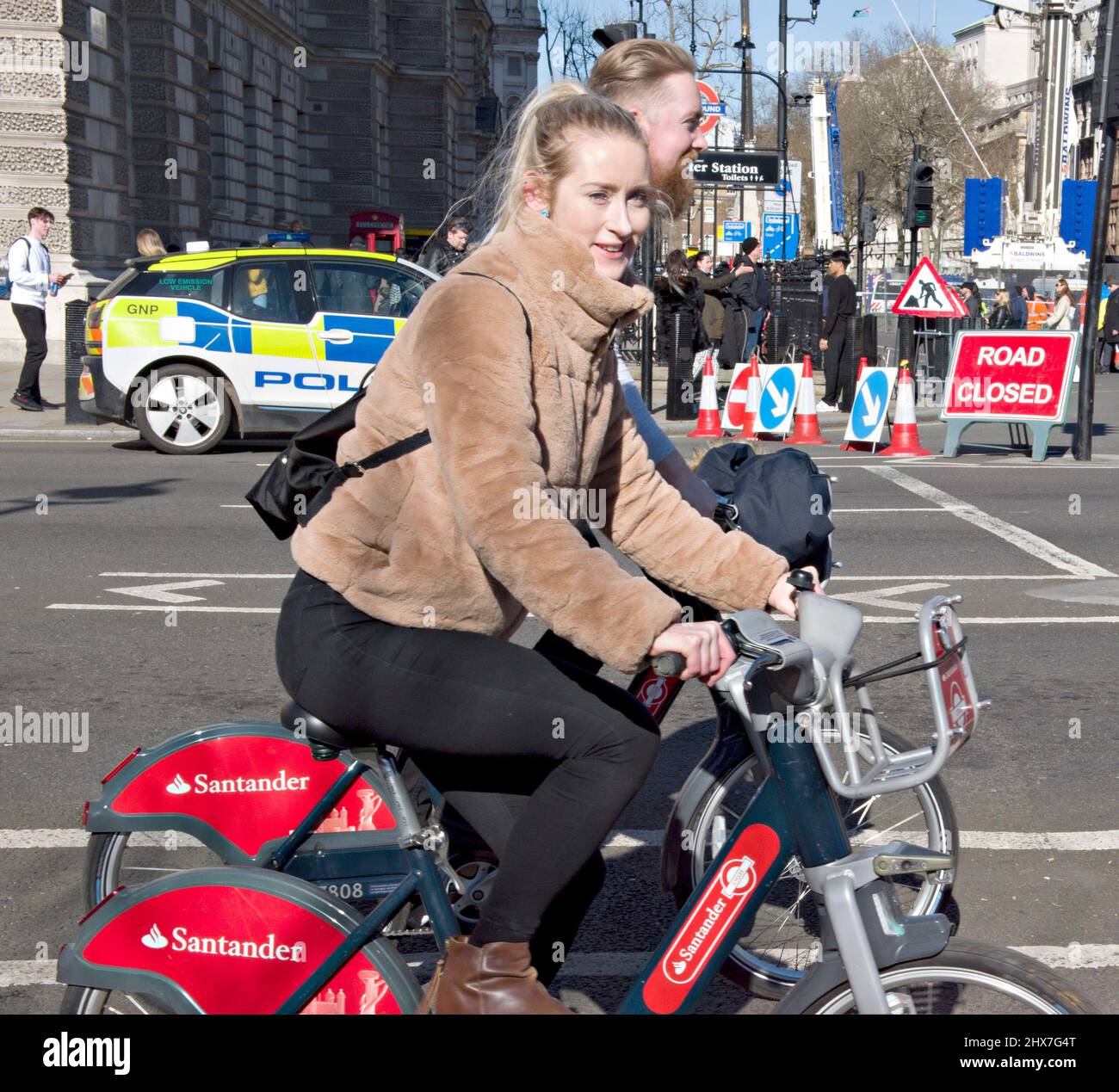 A couple using the bike hire service inLondon. Seen here in Westminster, central London. The bike hire scheme, promoting more green transport, was introduced in 2010; Barclays Bank being the first sponsor, and Santander from 2015. Although generally known as 'Boris bikes, after the London Mayor at the time; the concept was actually first promoted by the previous mayor, Ken Livingtone. Stock Photo