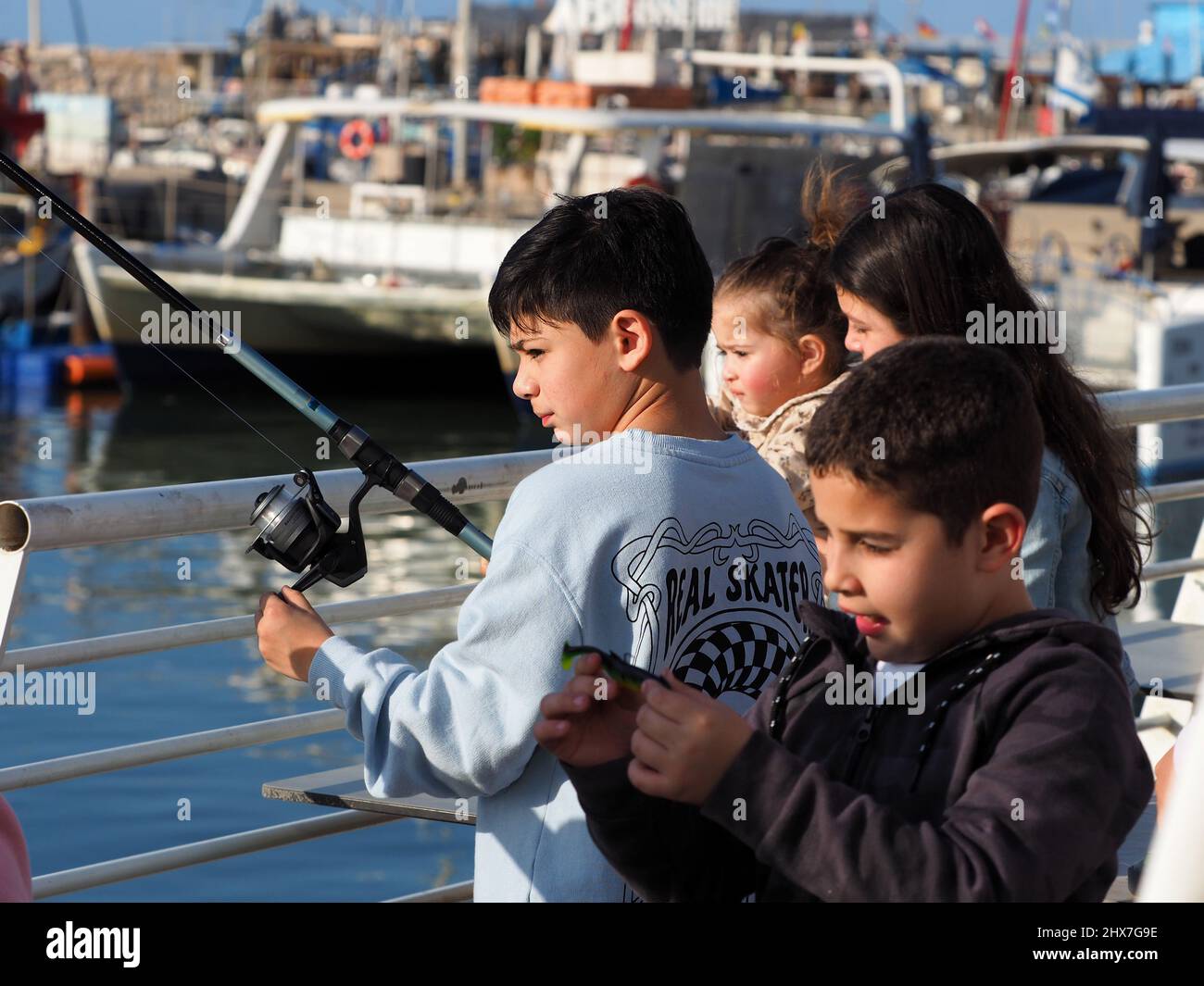 ASHKELON, ISRAEL - MARCH 04, 2022: Children go fishing in the port of Ashkelon. Focus on the boy with the fishing rod. Blurred background. Stock Photo