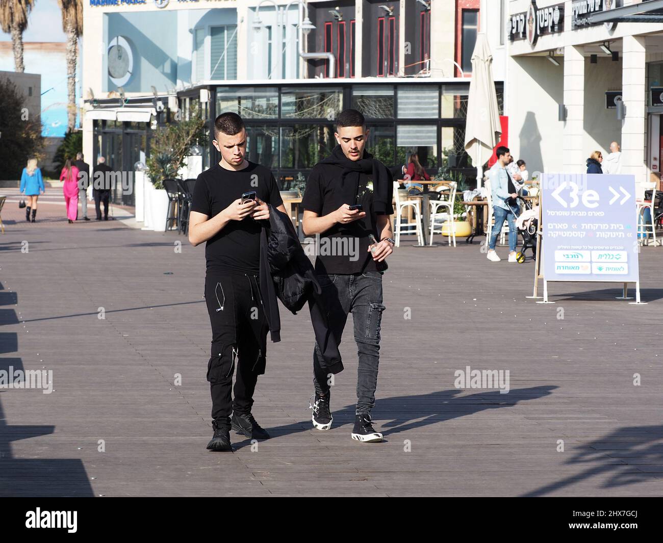 ASHKELON, ISRAEL - MARCH 04, 2022: young people looking into smartphones while walking on city street. Stock Photo
