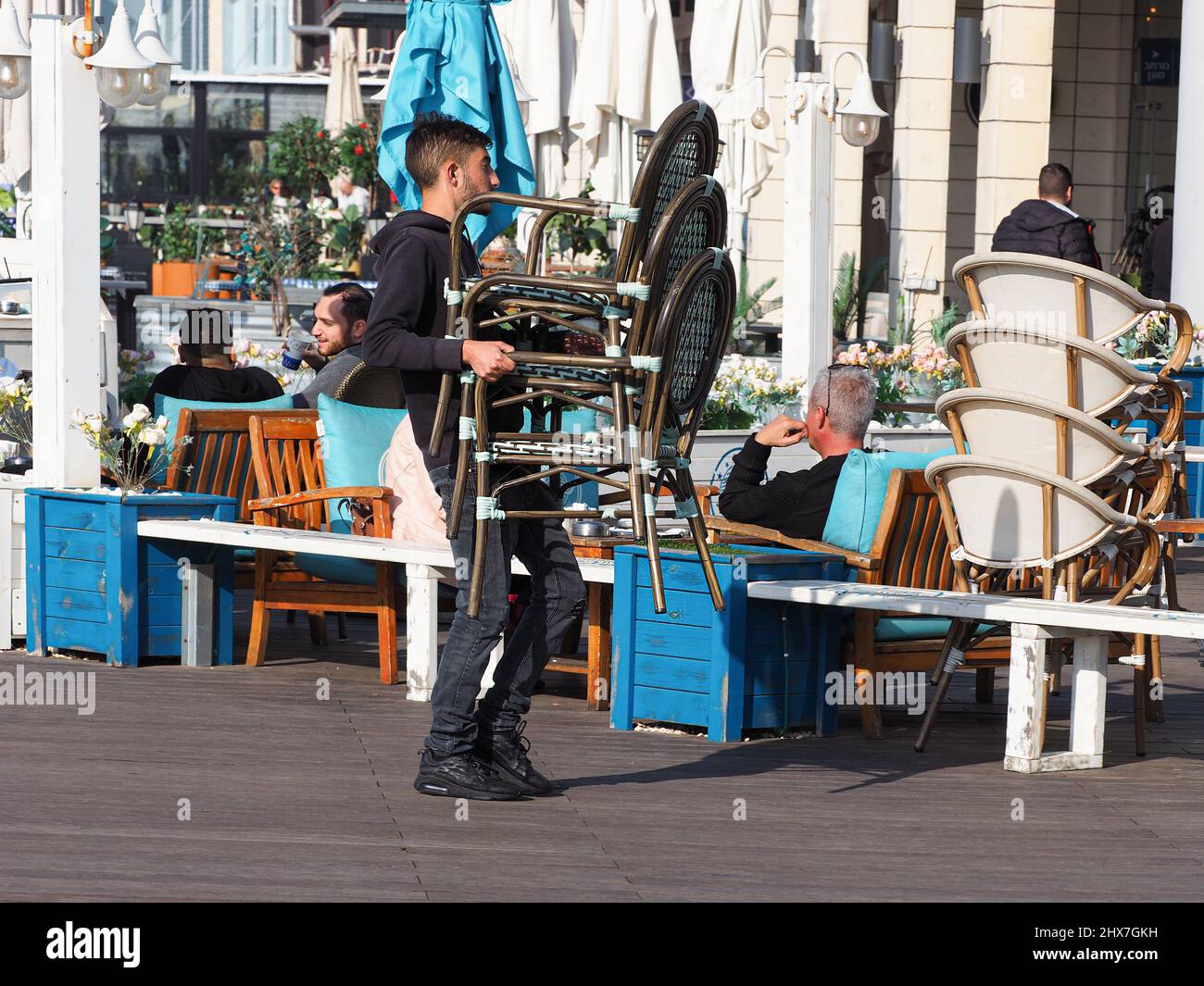 ASHKELON, ISRAEL - MARCH 04, 2022: A restaurant worker collects chairs in a street cafe. Stock Photo