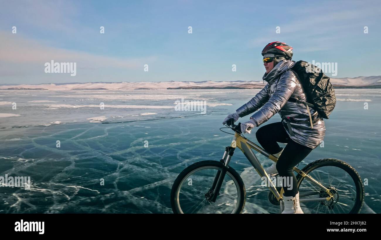 Woman is riding bicycle on the ice. Girl is dressed in a silvery down