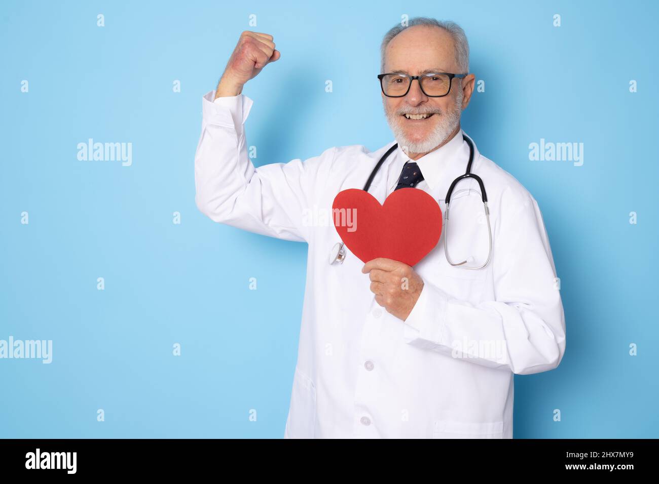 Senior age handsome grey-haired doctor man holding heart of red paper with a happy face standing and smiling with a confident smile showing strong ges Stock Photo