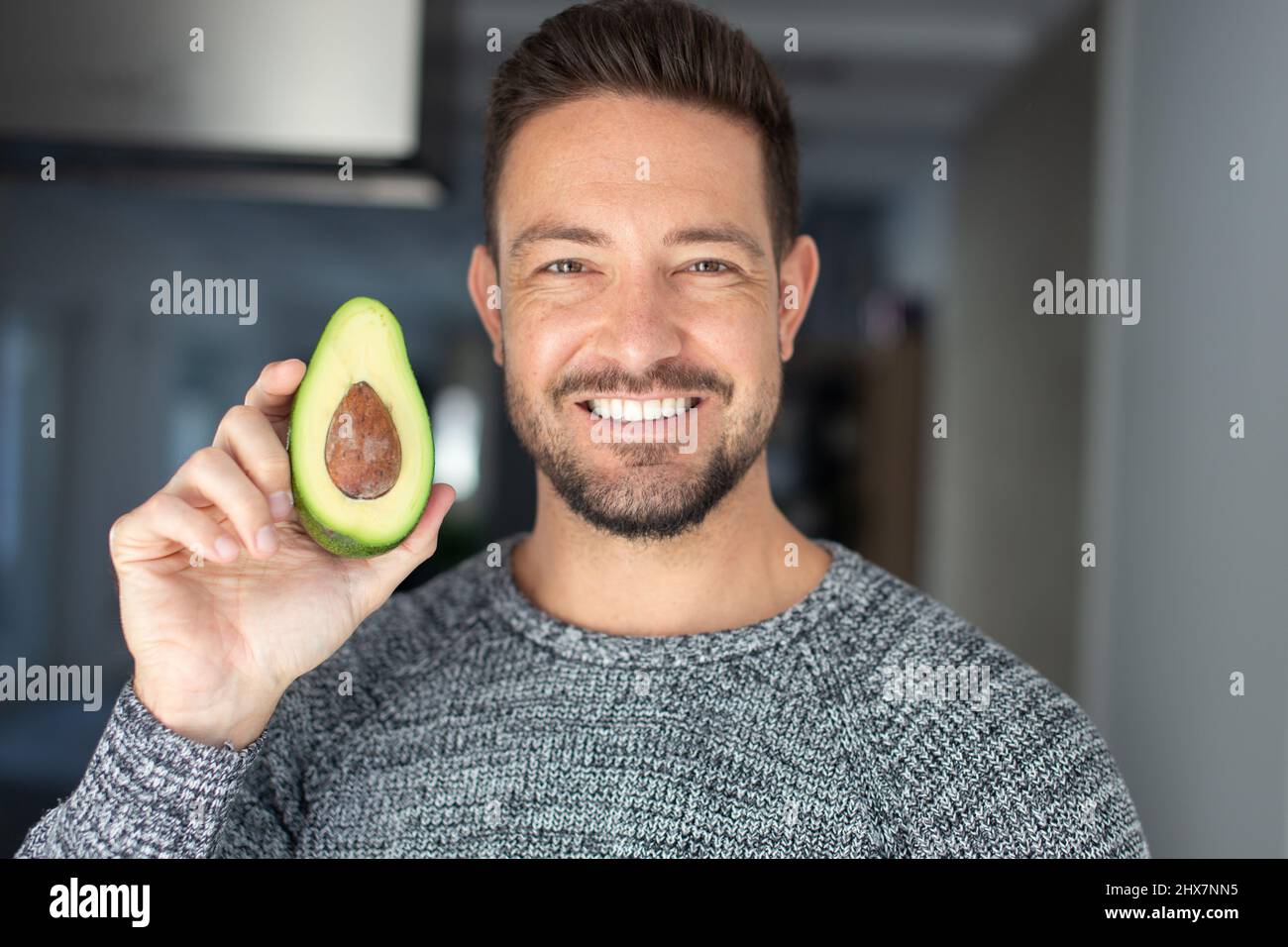 Young Caucasian 30s man holding halved avocado with toothy smile Stock Photo