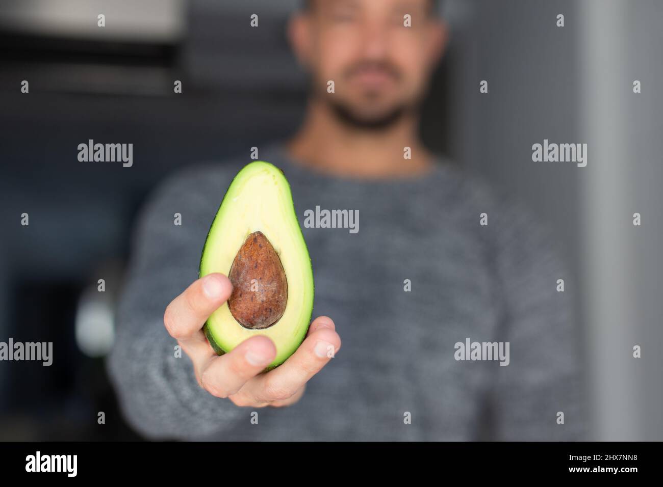 Young Caucasian 30s man holding halved avocado, selective focus Stock Photo
