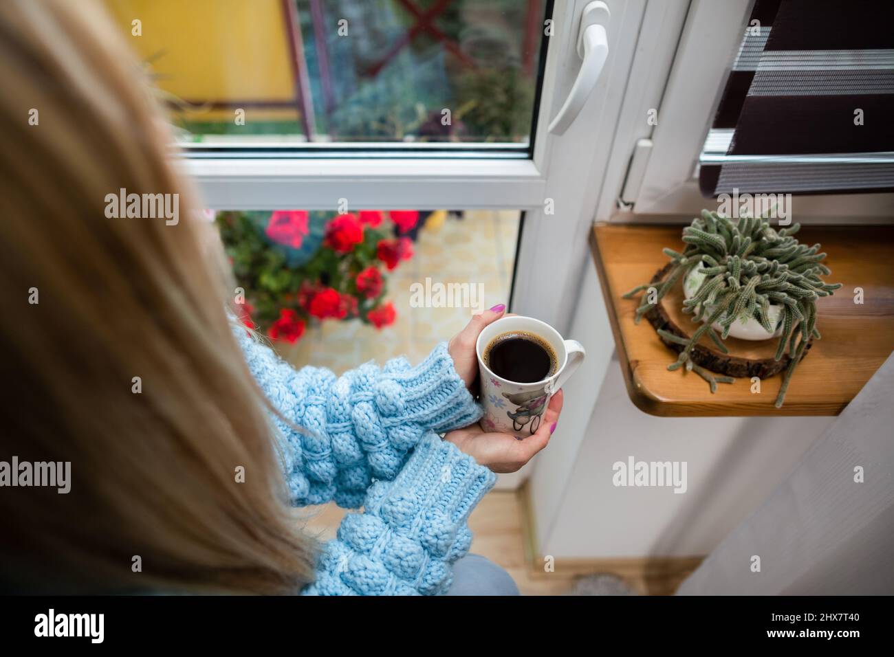 A woman sits at home holding a mug of hot coffee in her hands. Stock Photo
