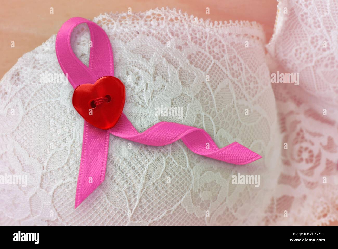 Pink ribbon with heart shaped button on white lace bra - Breast cancer concept Stock Photo