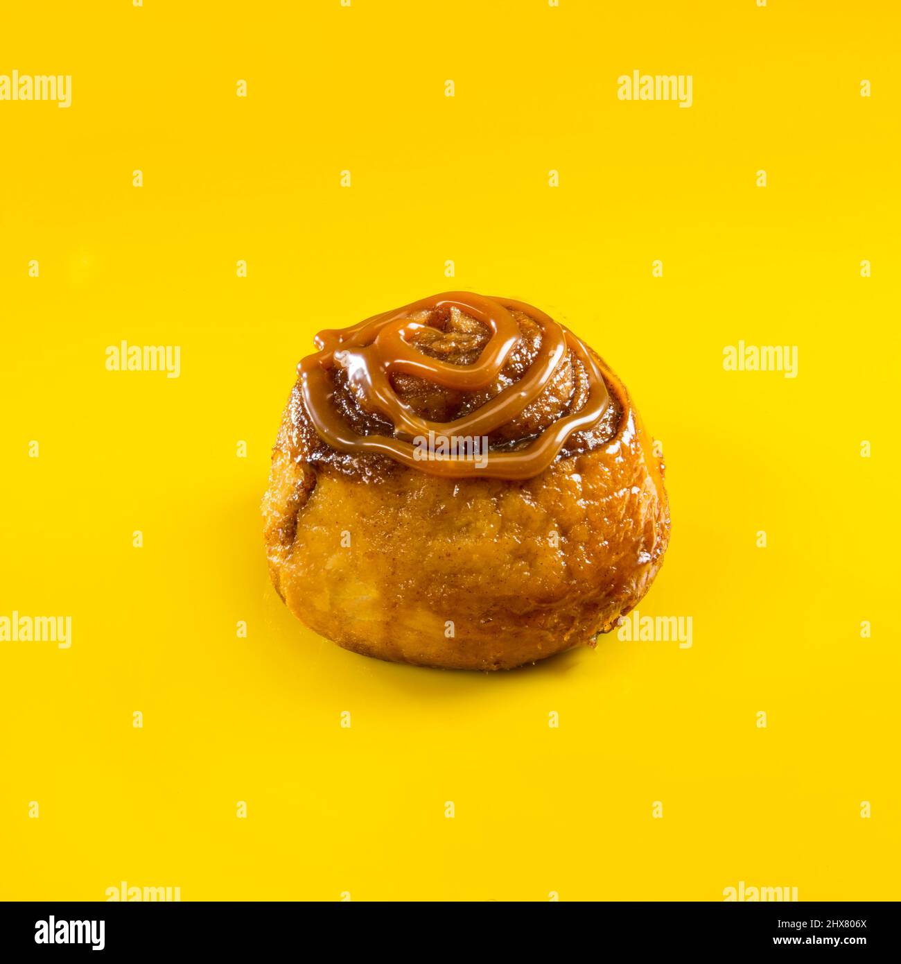 Cinnamon roll with caramel topping on yellow background Stock Photo