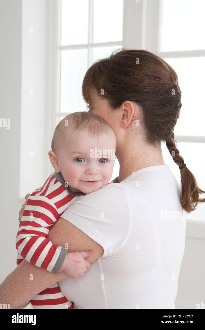Rear-side view of mother holding baby boy against one shoulder Stock ...