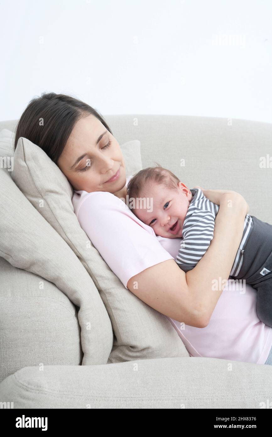 Woman reclining on sofa with laughing baby boy cuddled on his front to