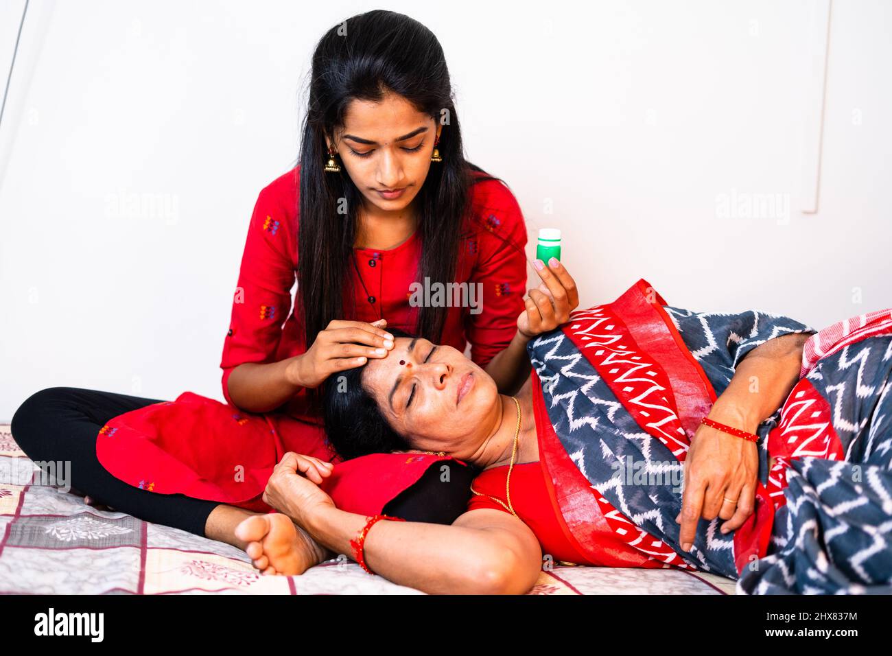 teenage daughter taking care of her by applying balm to forehead to sick mother while sleeping on daughters lap - concpet of caretaker, consoling Stock Photo