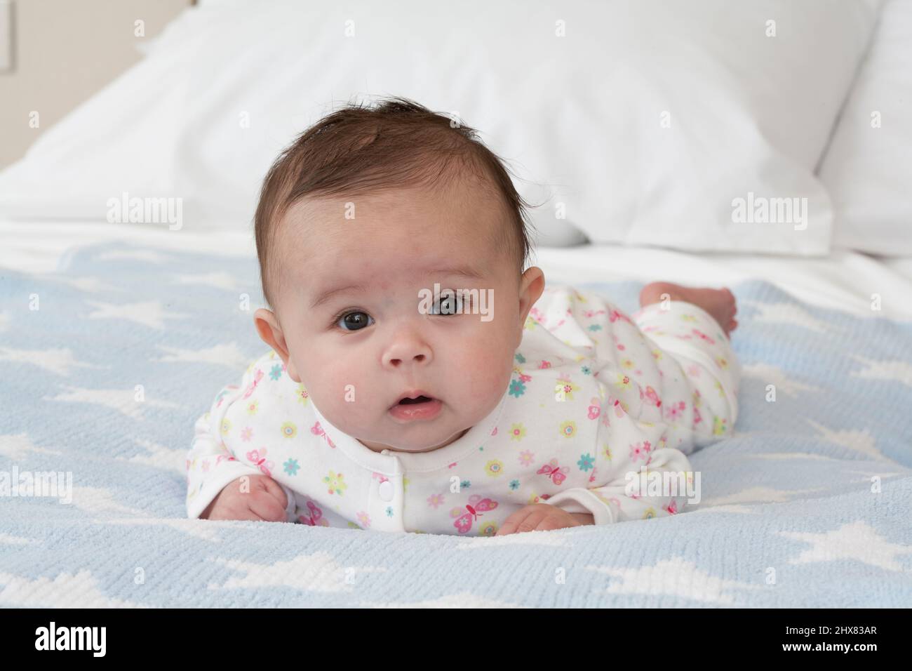 Baby girl lying on her front on a bed with head raised and alert ...