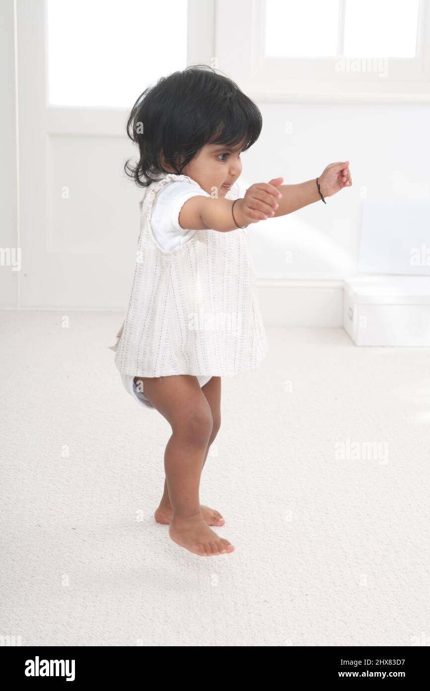 Toddler girl stood on carpeted floor with arms raised in dancing motion Stock Photo