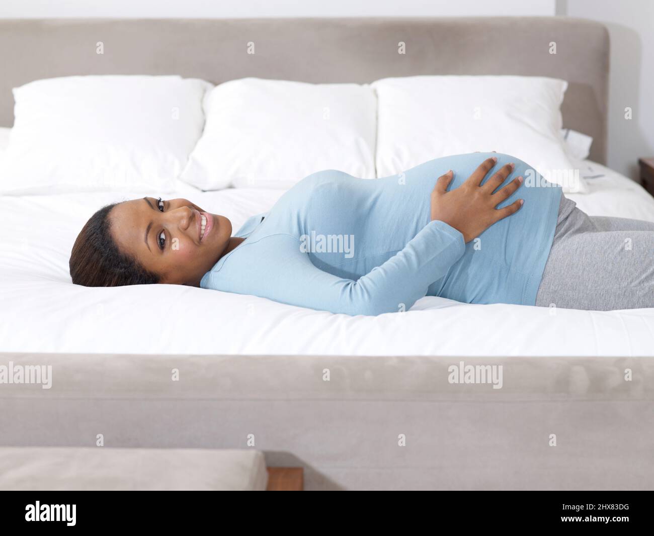 Pregnant woman lying on her back on a bed, touching her belly Stock