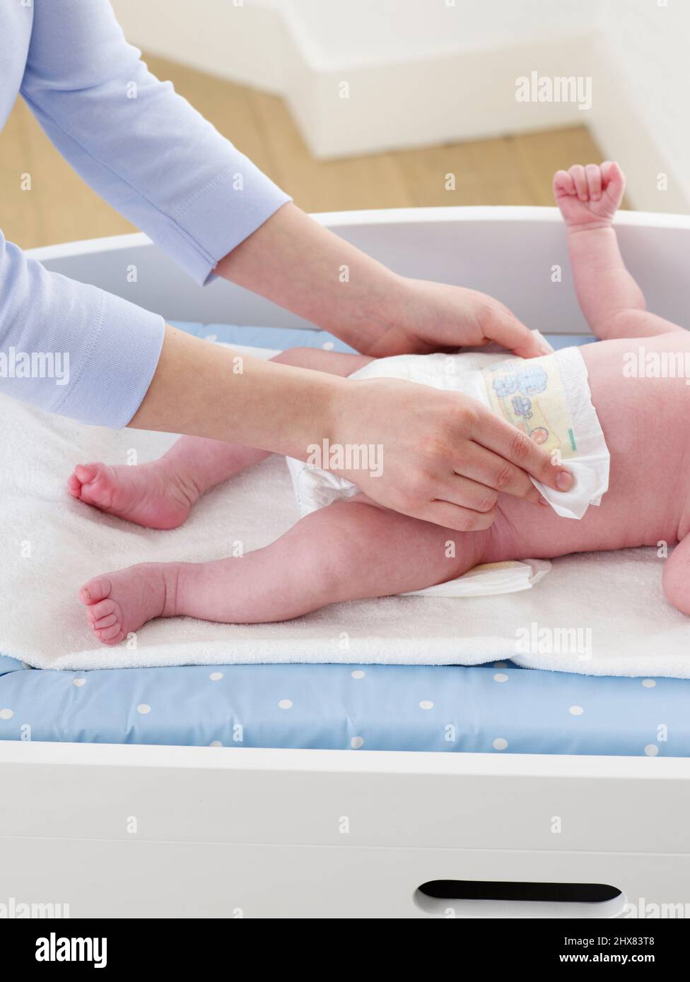 Mother changing nappy of baby boy lying on changing mat, side view