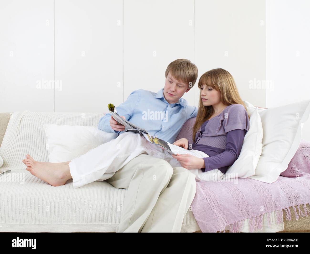 Young pregnant woman sitting on sofa with legs laying across lap of man