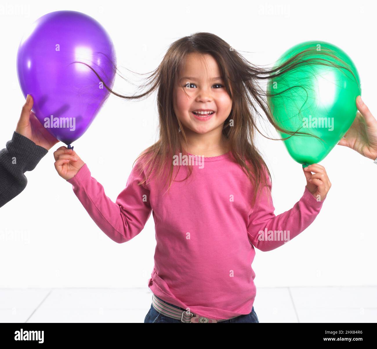 Girl (3.5 years) standing laughing as her hair sticks with static electricity to two balloons Stock Photo
