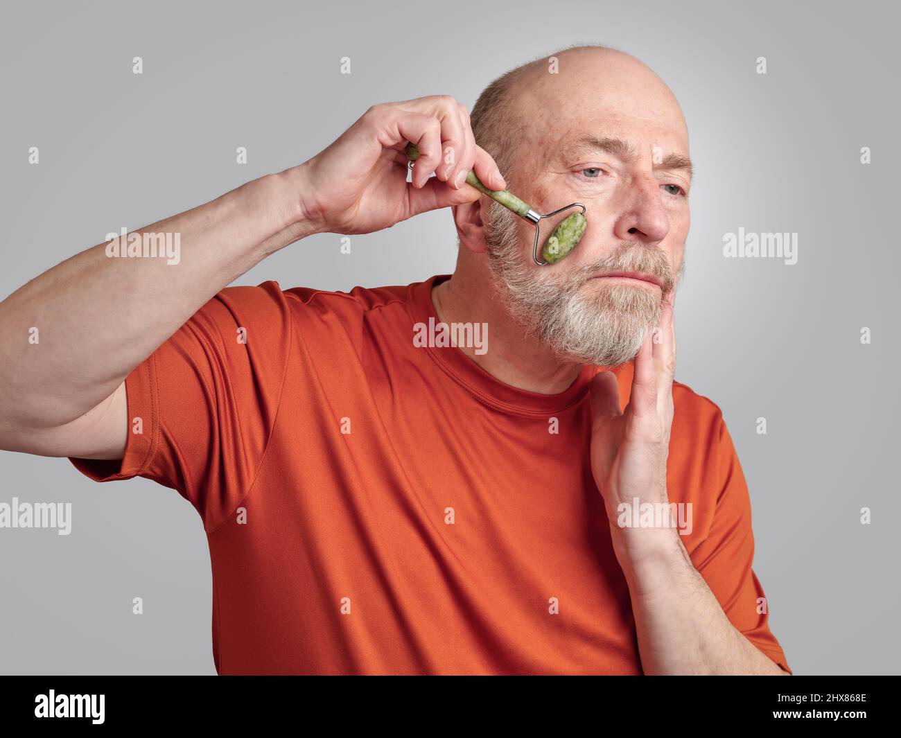 senior man is using a jade stone roller for a face massage, skin care routine concept Stock Photo