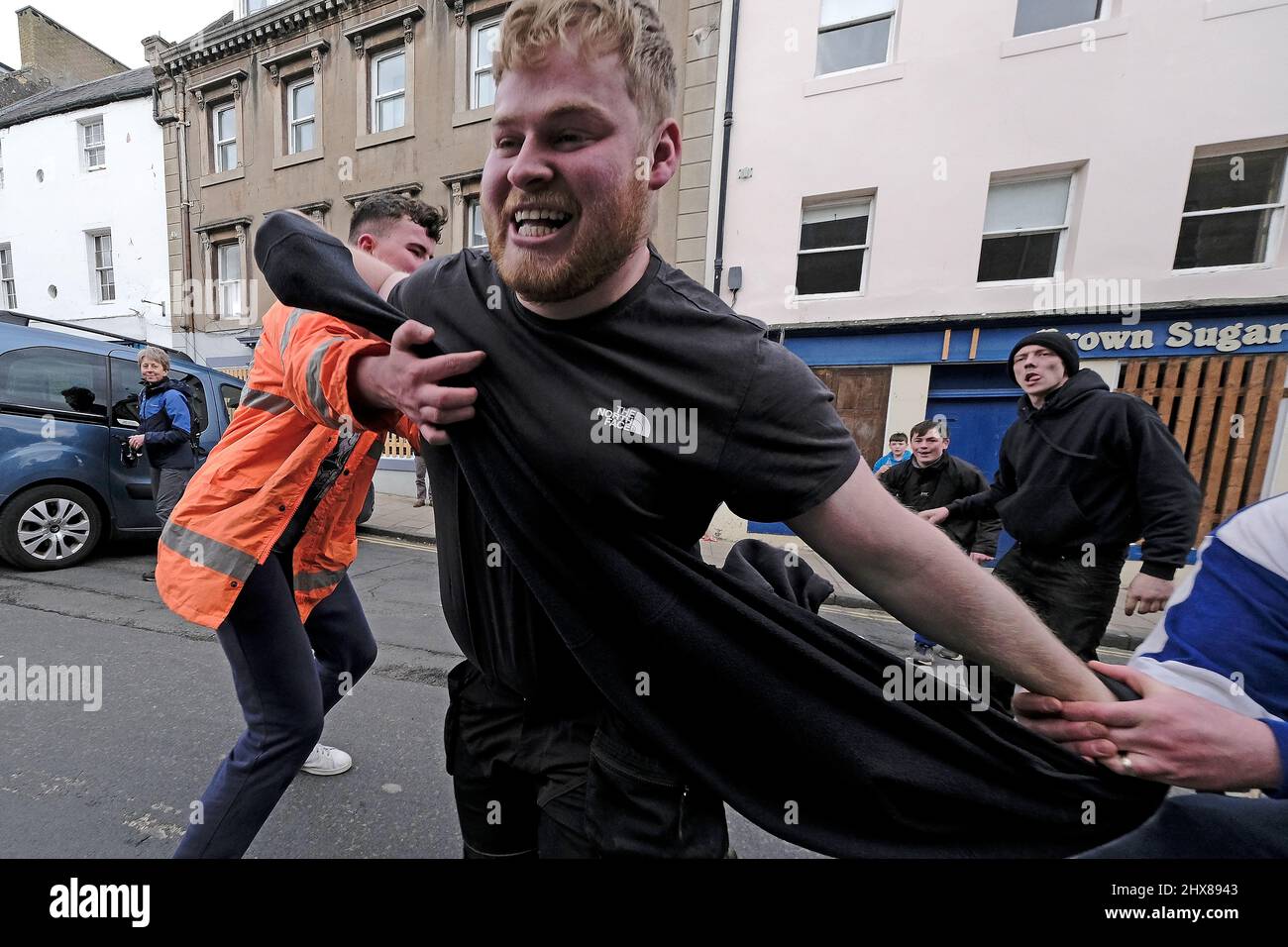 Jedburgh, Thursday 10 March 2022. A man is tackled while he carries the “Ba” during the annual 'Fastern Eve Handba' event in Jedburgh's High Street in the Scottish Borders on March 10, 2022 in Jedburgh, Scotland. The annual event, which started in the 1700's, takes place today and involves two teams, the Uppies (residents from the higher part of Jedburgh) and the Doonies (residents from the lower part of Jedburgh) getting the ball to either the top or bottom of the town. The ball, which is made of leather, stuffed with straw and decorated with ribbons is thrown into the crowd to begin the game Stock Photo