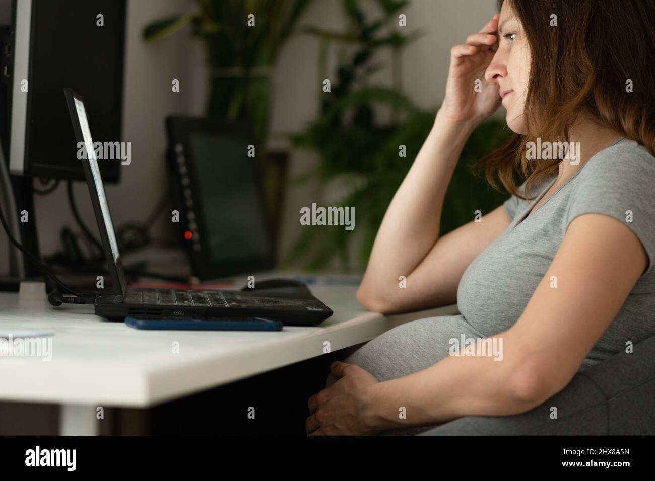 A pregnant woman is working on a laptop. The hand is on the stomach