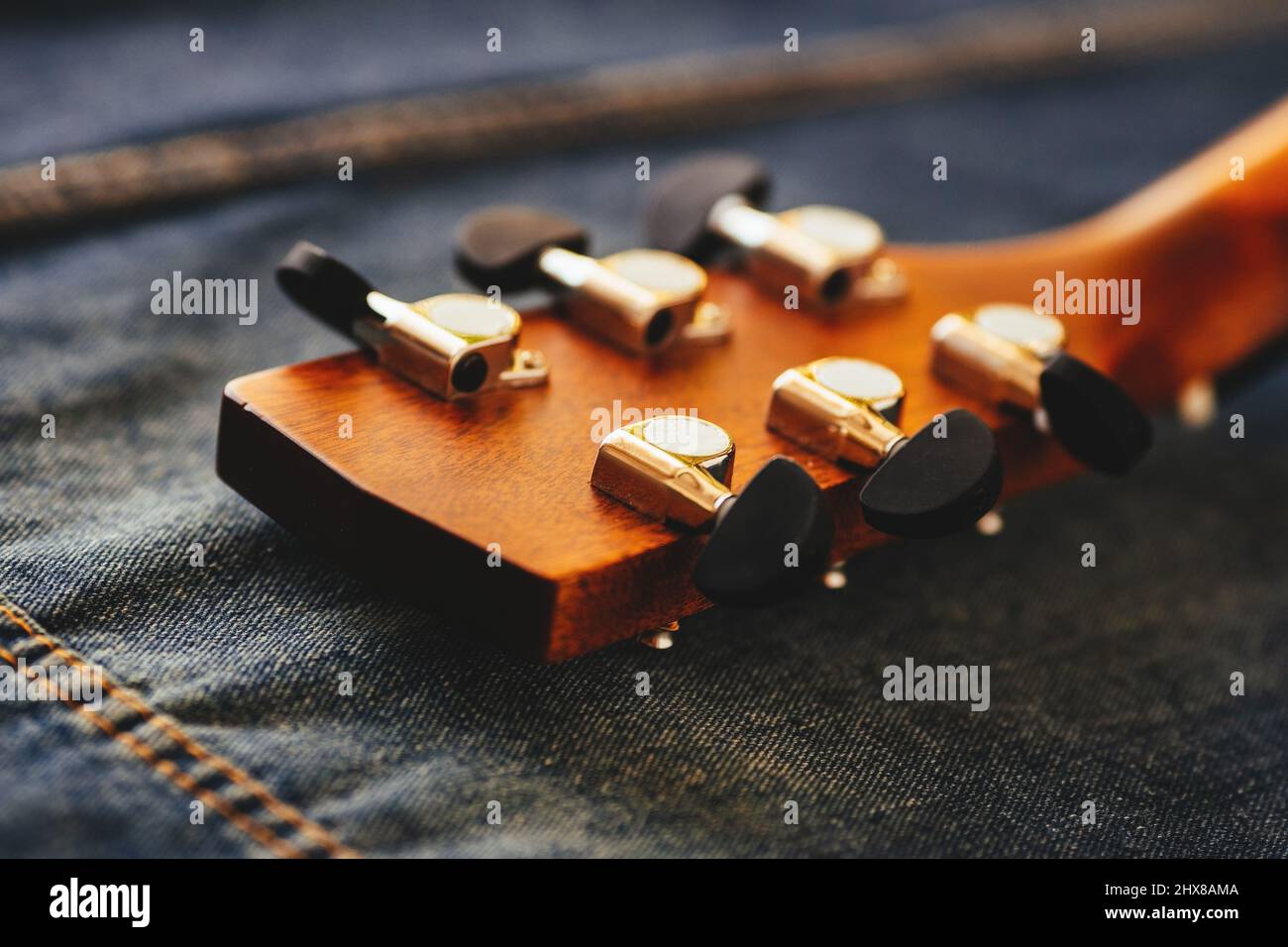 Neck of acoustic guitar is close-up on denim fabric. Hipster culture. Background. Musical instrument. Learning to play guitar. Stock Photo